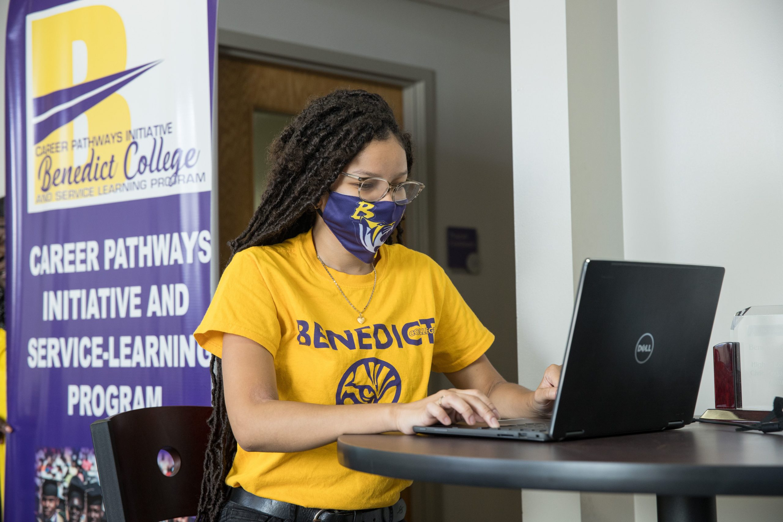 Student wearing a BC t-shirt and mask works on a laptop.